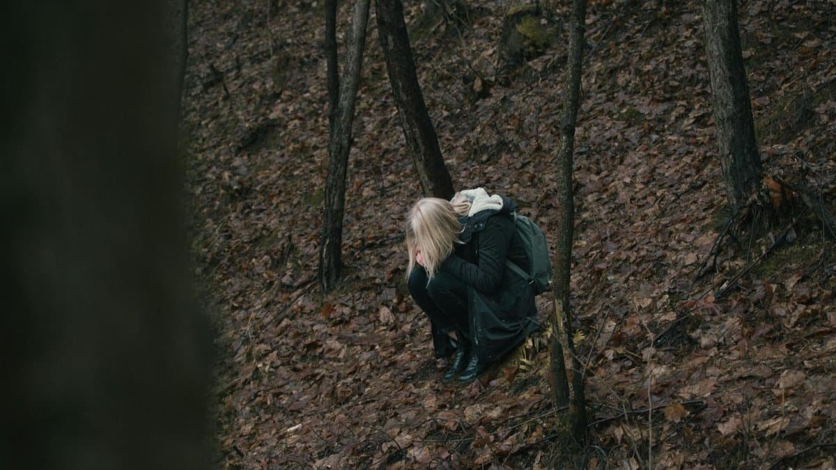 A person sitting alone in a quiet forest, immersed in thought during autumn season.
