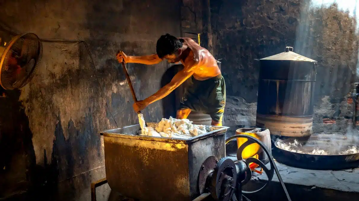 Man stirring a vat in an industrial soap factory, illuminated by natural light.