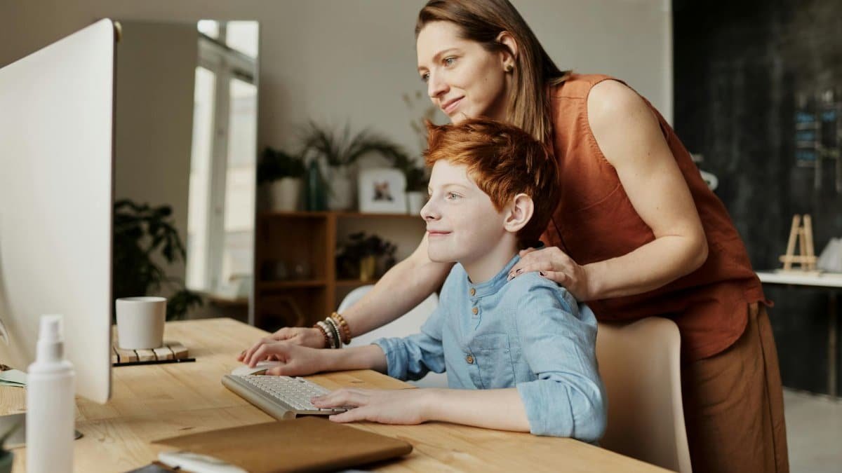 A mother and her child smiling while using a computer at home, focused on learning.