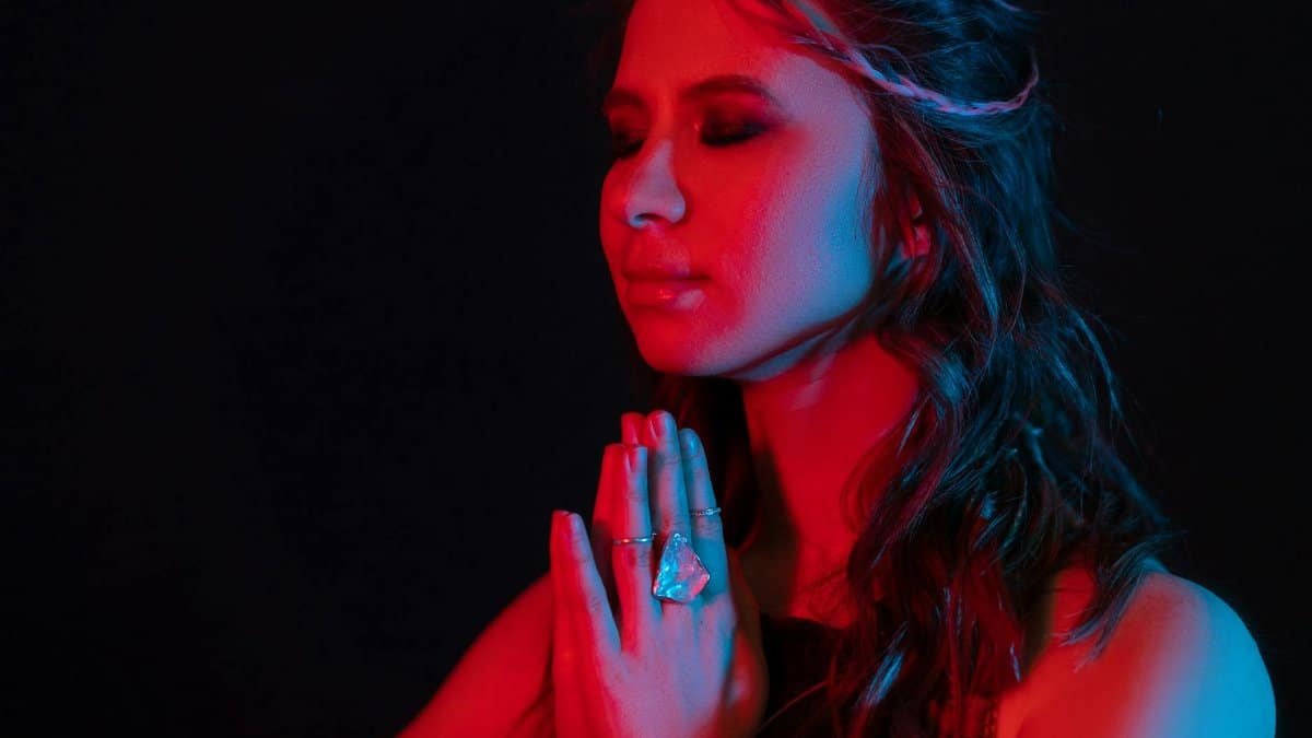A woman meditates with hands in prayer, bathed in contrasting red and blue light.