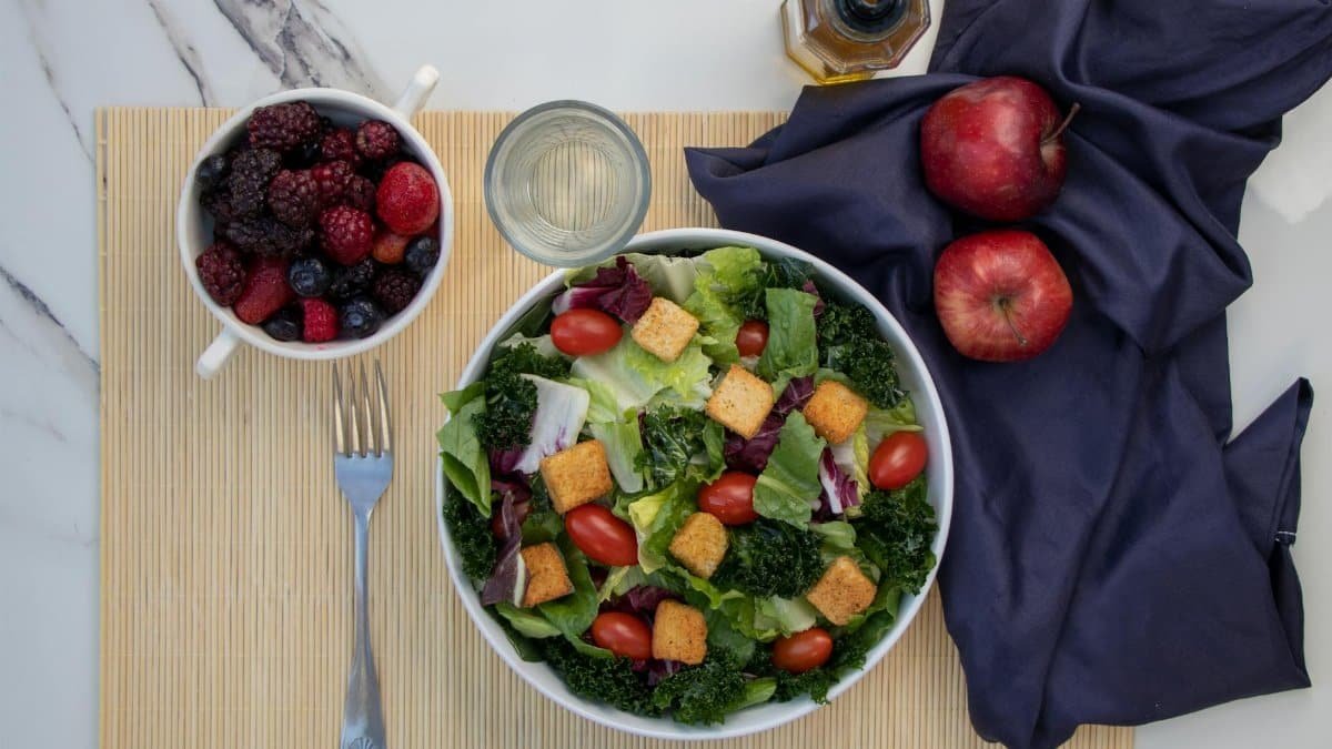 A vibrant salad with kale, cherry tomatoes, and apples, paired with fresh berries for a healthy meal.