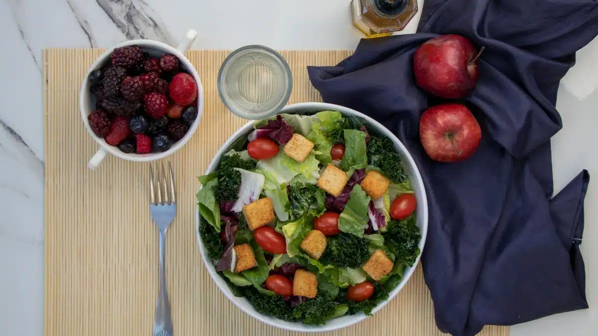 A vibrant salad with kale, cherry tomatoes, and apples, paired with fresh berries for a healthy meal.