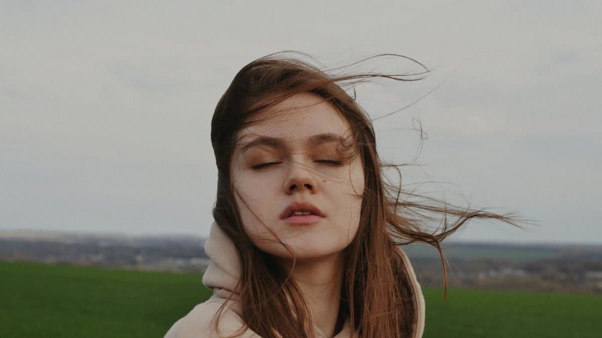 Young woman with closed eyes enjoying the wind in an open field. A moment of peace and serenity.