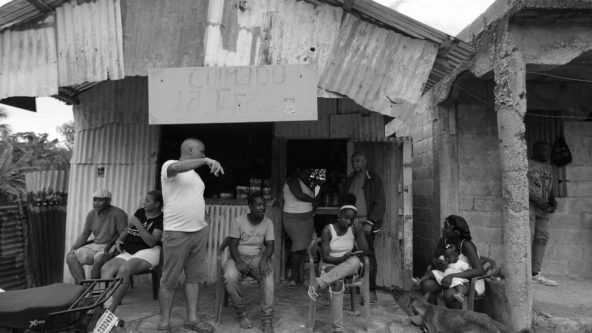 A group of people gather outside a rustic community shop, displaying everyday life in a rural setting.