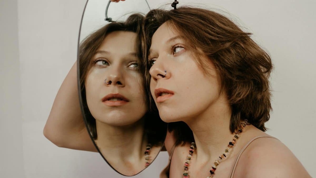 Close-up of a woman with a mirror reflection, highlighting her contemplative expression.
