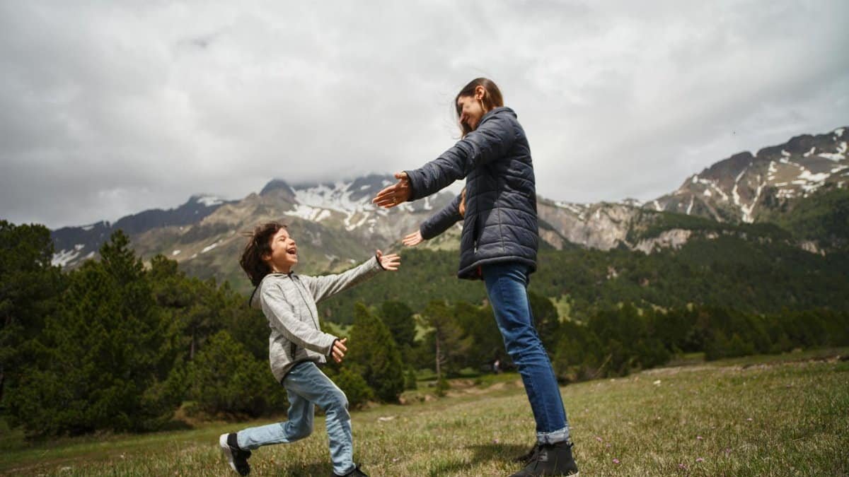 A mother and child embrace joyfully in a lush mountain setting, capturing a moment of happiness and love.