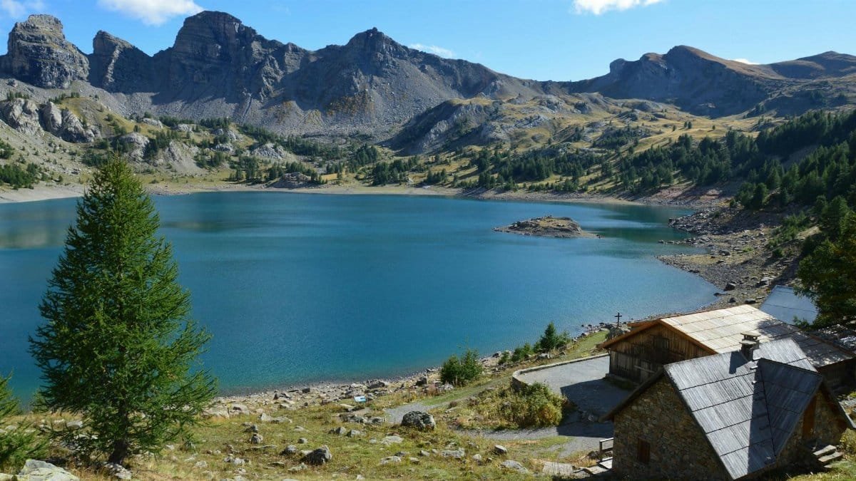 Stunning mountain lake with wooden cabins surrounded by rocky peaks and lush greenery.