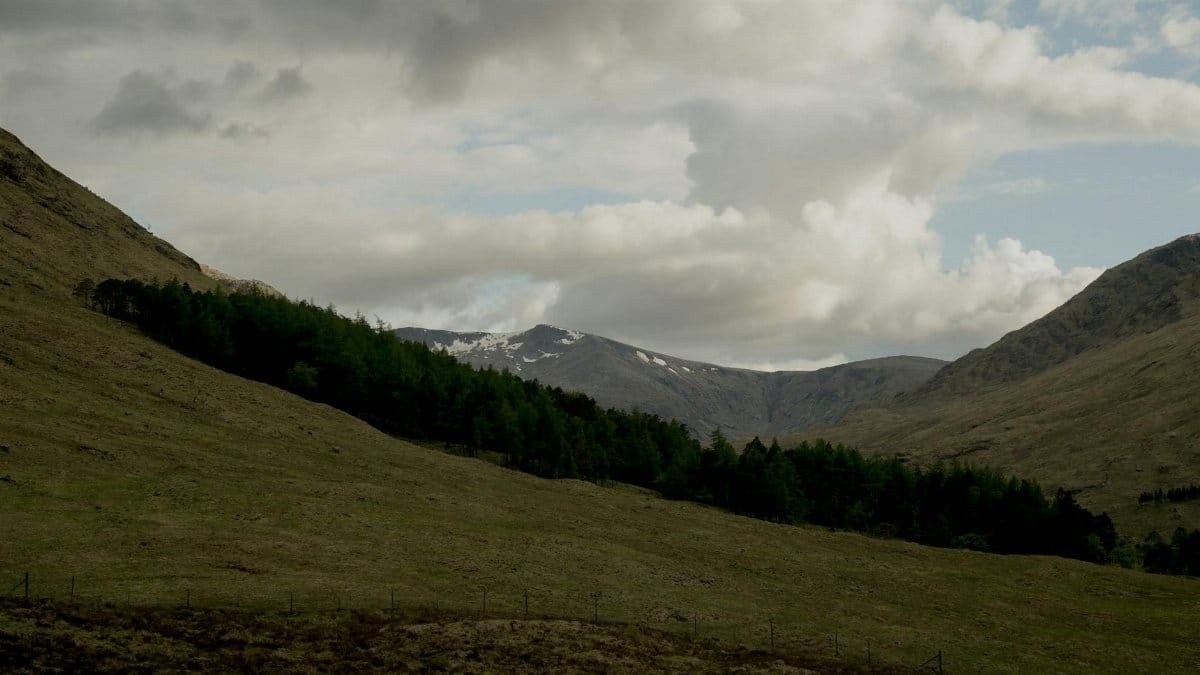 A tranquil view of a mountain valley with lush trees and dramatic clouds, creating a peaceful natural landscape.