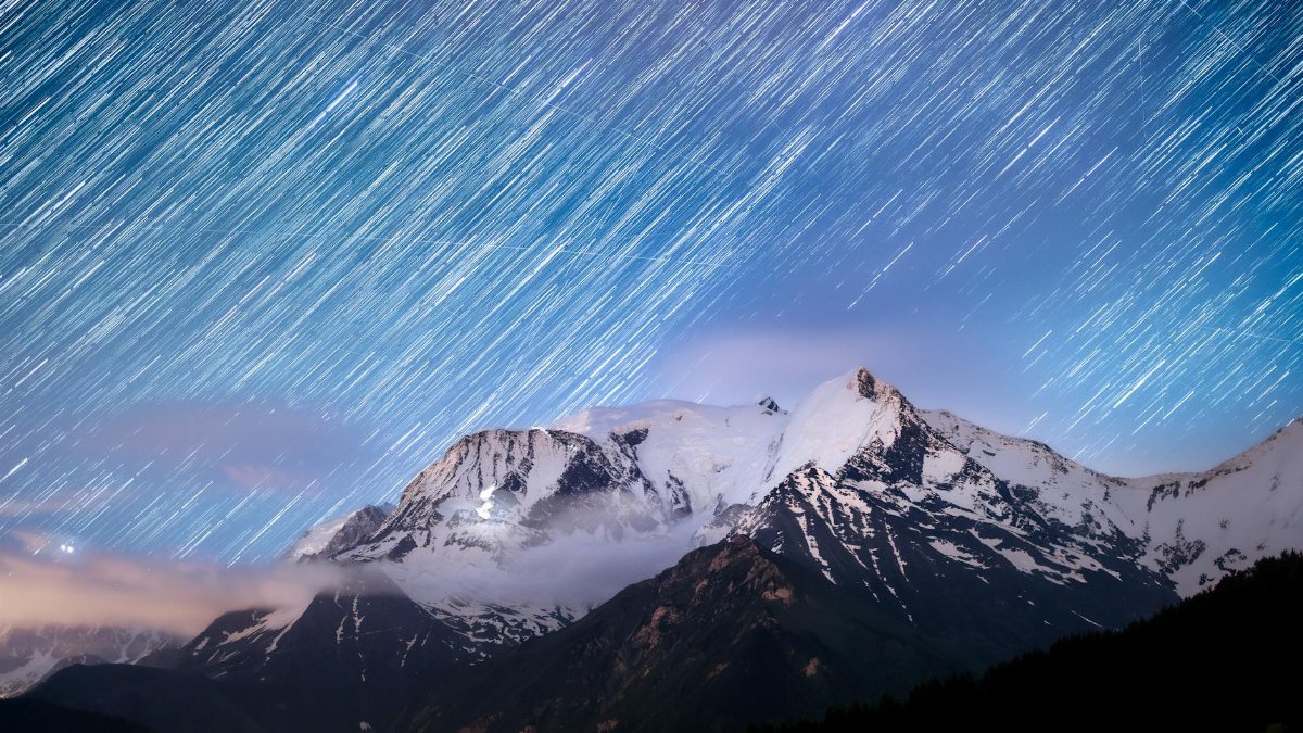 Captivating view of star trails over Mont Blanc with a vibrant sunrise, showcasing natural beauty.