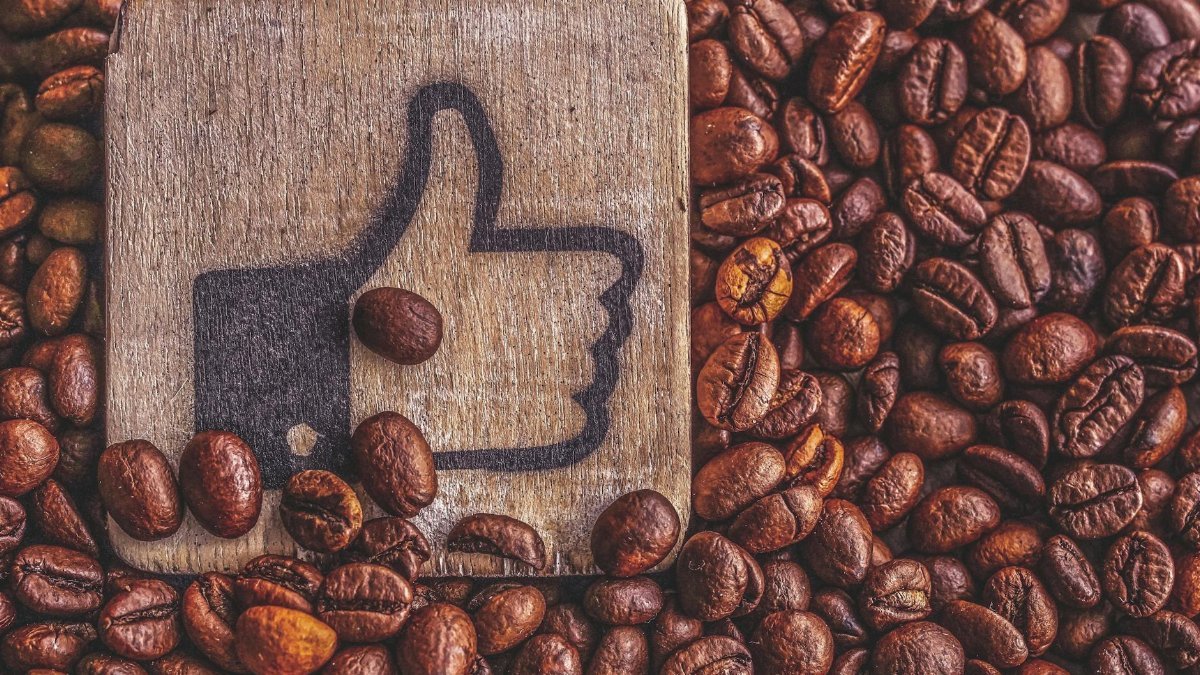 A wooden thumbs up symbol resting on a pile of roasted coffee beans, representing appreciation.