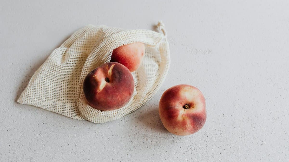 Three fresh peaches in a sustainable net bag on a white background, promoting zero waste.