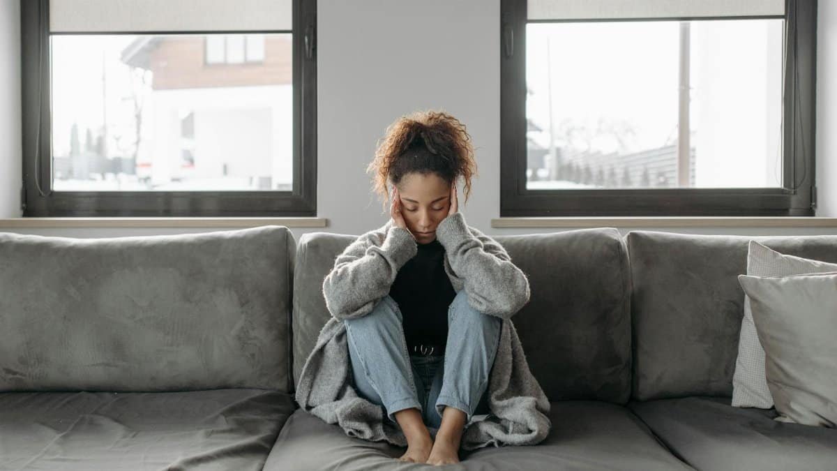 A woman sits on a sofa looking unwell, emphasizing a sense of illness or fatigue indoors.