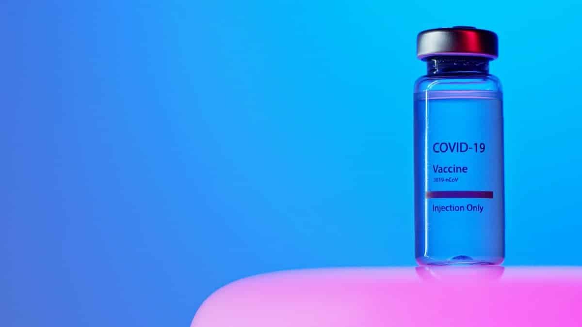 Close-up of a COVID-19 vaccine vial on a vibrant blue and pink background.
