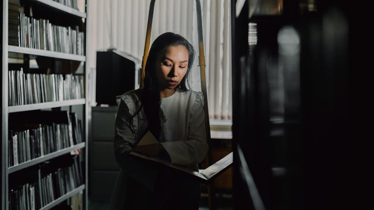 A woman deeply absorbed in a book within the dim light of a quiet library.