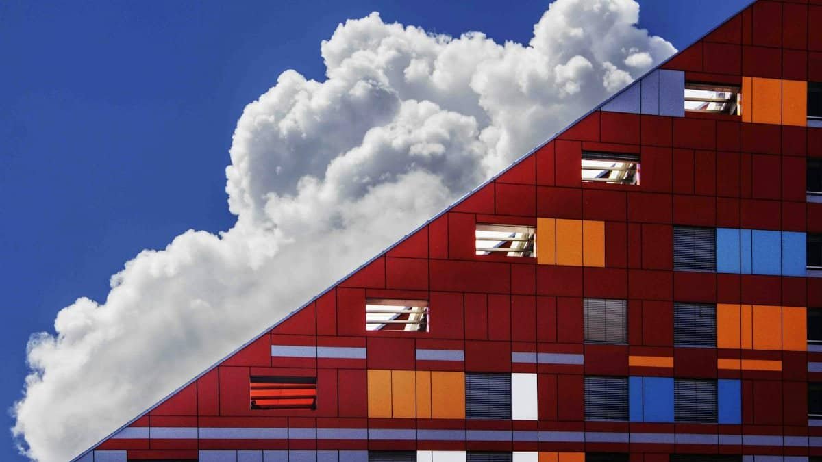 Colorful modern building facade against a backdrop of dramatic clouds and bright blue sky.