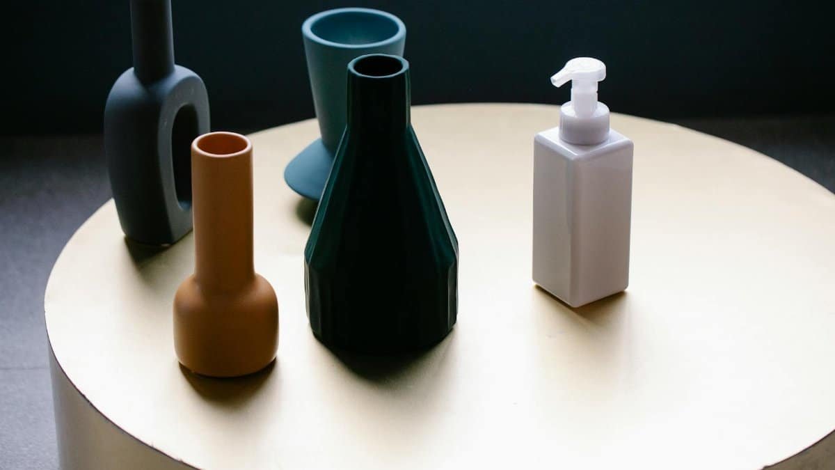 From above of white pump bottle of cosmetic lotion placed on round table near set of elegant vases of various shapes