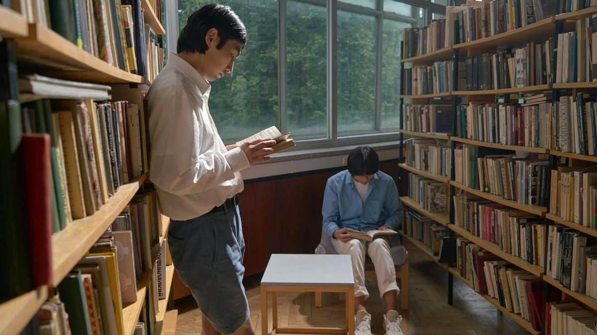 Two individuals reading in a quiet library setting with abundant natural light.