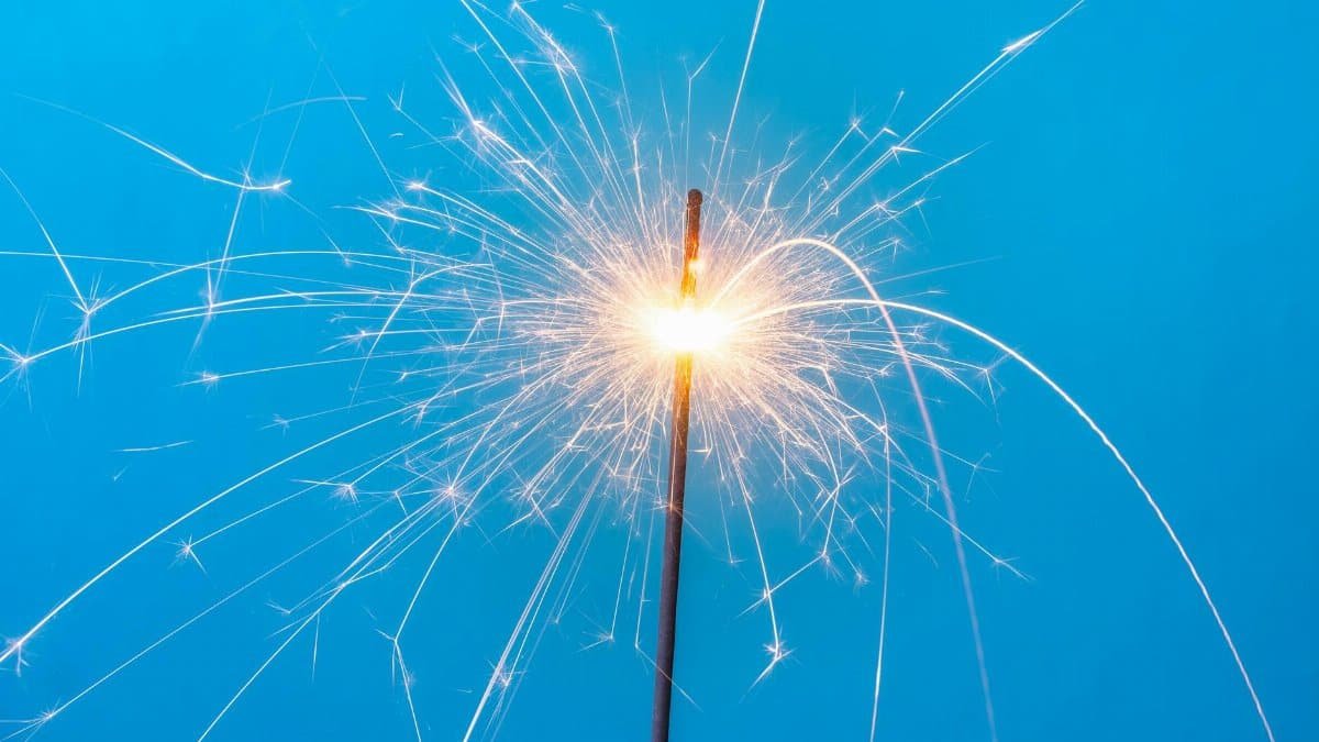 Close-up of a sparking sparkler against a blue background, symbolizing celebration and joy.