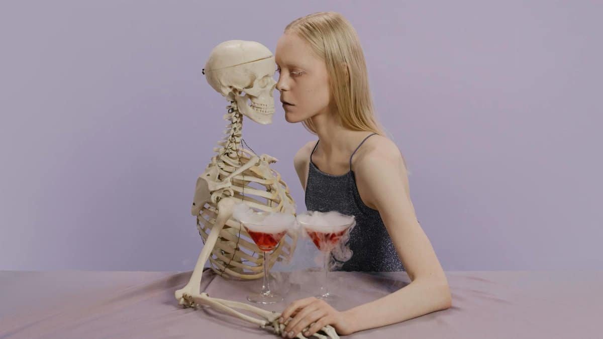A whimsical Halloween-themed photo of a woman posing with a skeleton and cocktails.