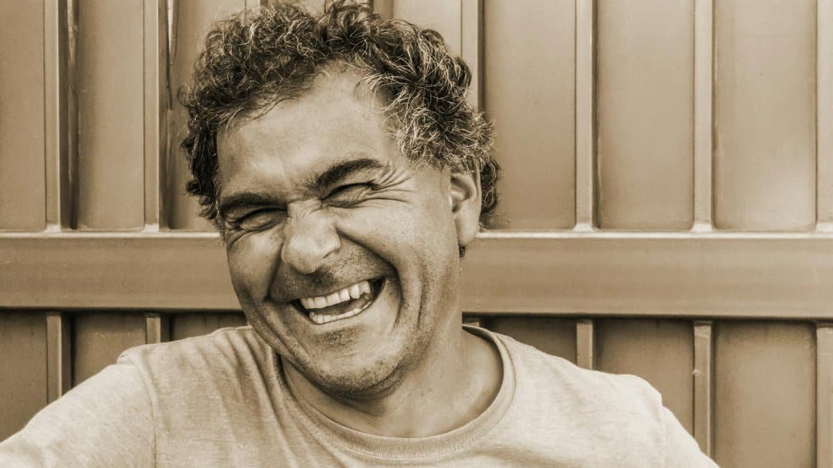 Close-up sepia portrait of a happy, laughing man against a textured background.