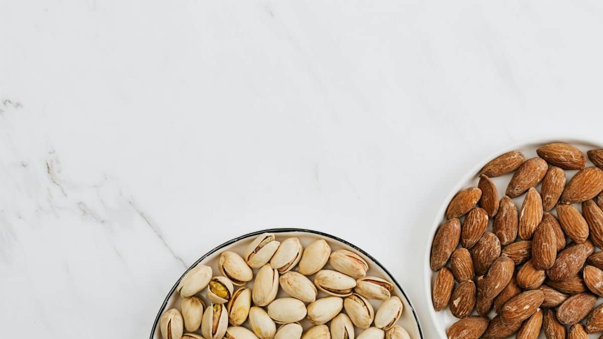 Overhead view of almonds and pistachios on white marble for healthy snack ideas.
