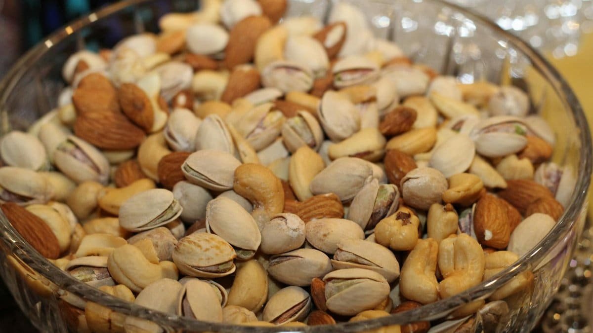 A close-up view of a glass bowl filled with various mixed nuts, including almonds, cashews, and pistachios.