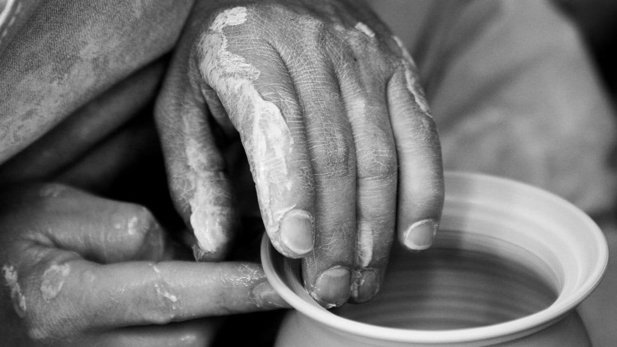 Artistic black and white close-up of hands shaping clay pottery on a wheel.
