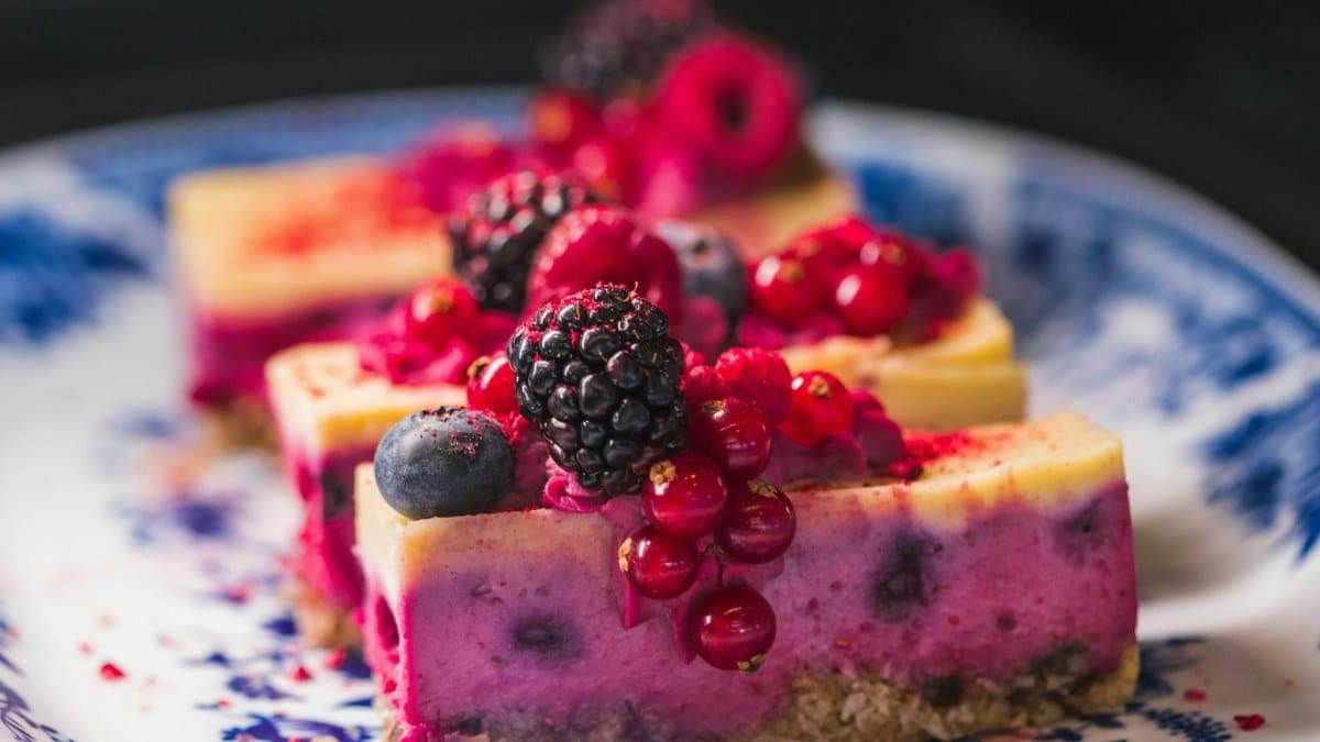 Sliced berry cheesecake topped with vibrant fresh berries and served on a decorative plate.