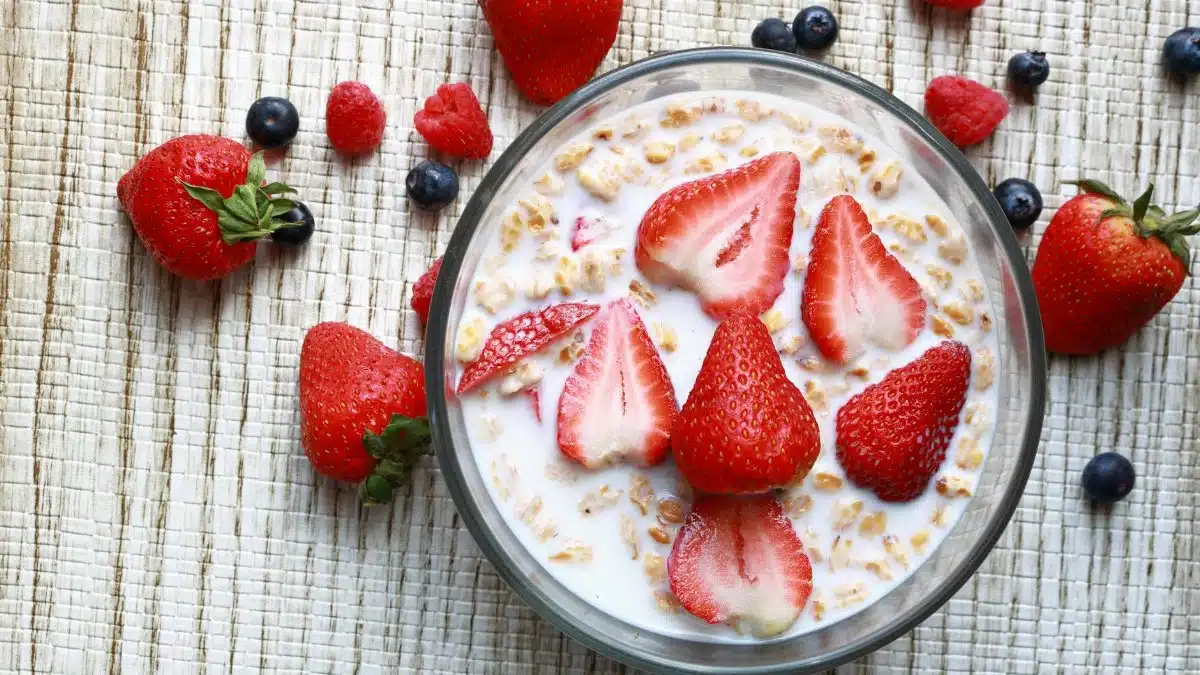 Top view of a cereal bowl with fresh strawberries, blueberries, and milk on a textured surface.