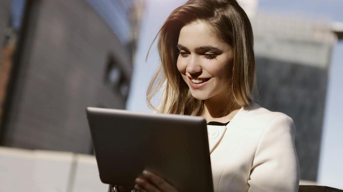 A woman joyfully using a digital tablet outdoors in the city during the day.