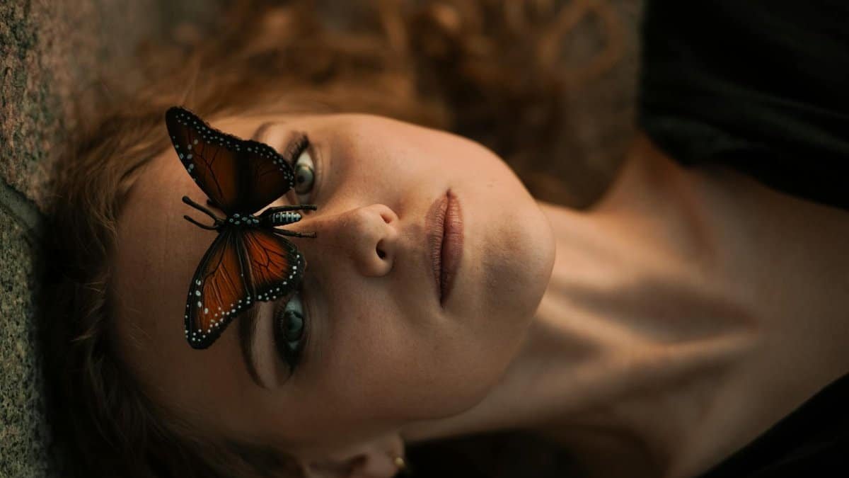 A captivating close-up of a woman with a monarch butterfly on her face, conveying serenity.