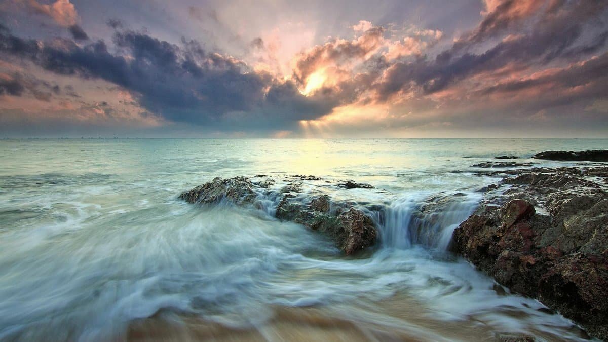 Beautiful sunrise over ocean rocks with waves crashing, capturing the serenity and power of nature.