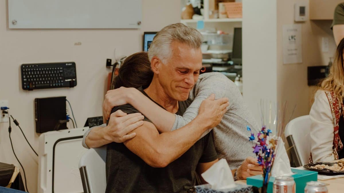 Emotional embrace among colleagues during a heartfelt gathering in an office setting.
