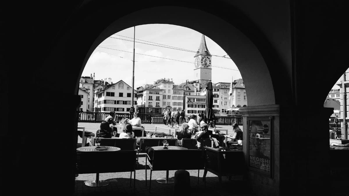 Arched view of Zurich with people dining, highlighting historic architecture.