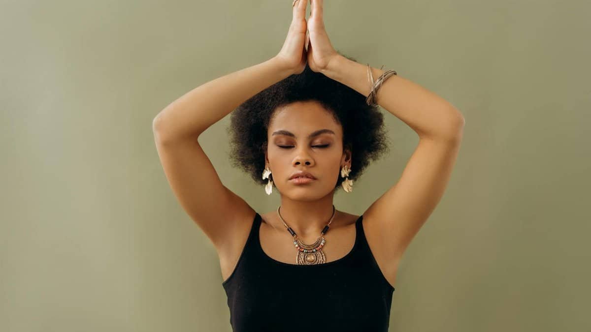 A woman in a black top meditates with closed eyes and hands in prayer pose, radiating calmness.