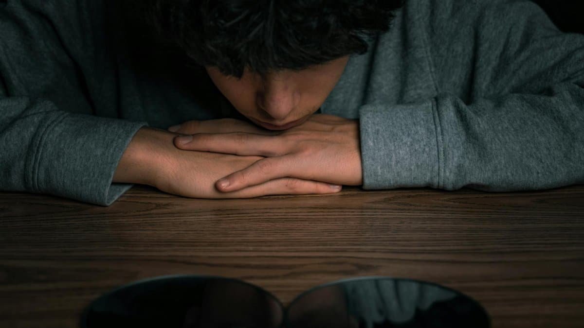 A young boy looking at his reflection in mirrors on a wooden table, deep in thought.