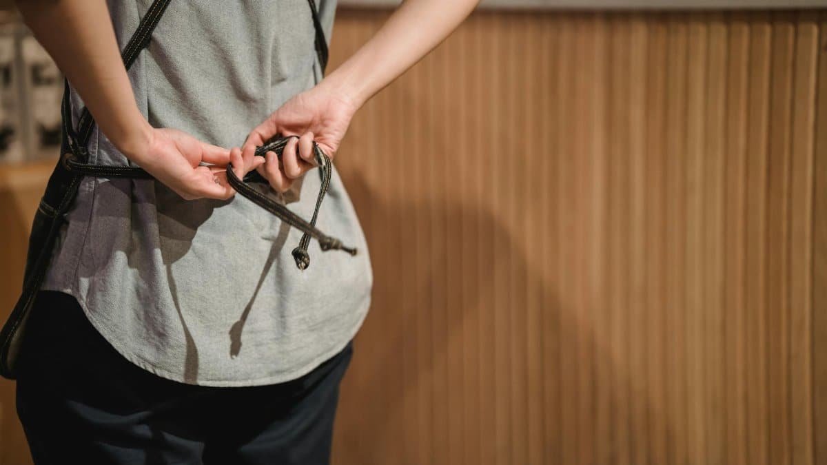 A barista adjusting an apron strap while preparing to work in a cozy cafe environment.