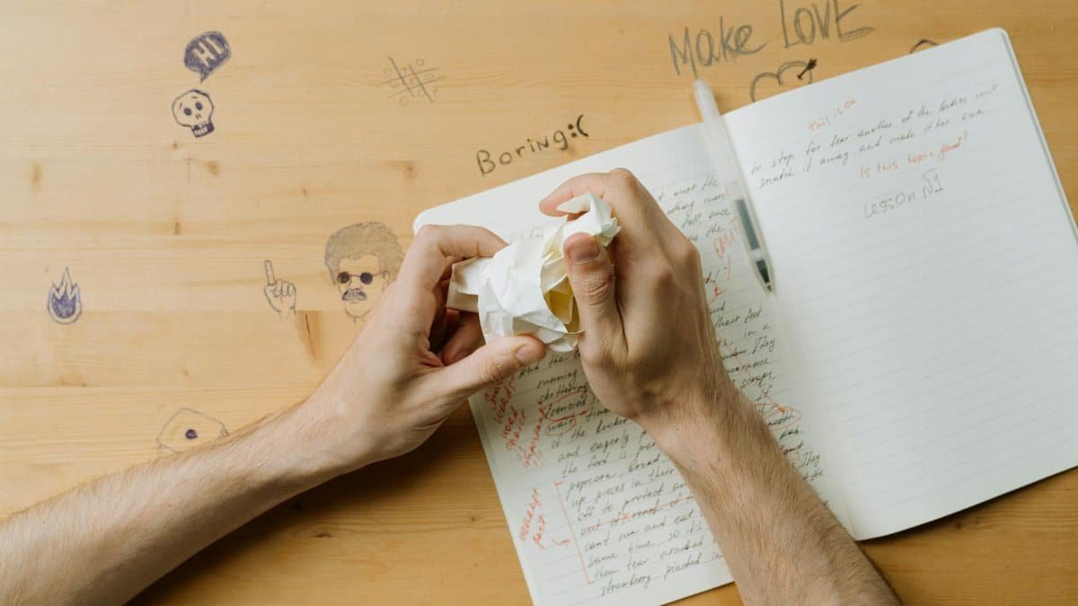 Hands crumpling paper over a notebook showing creative frustration at a writing desk.