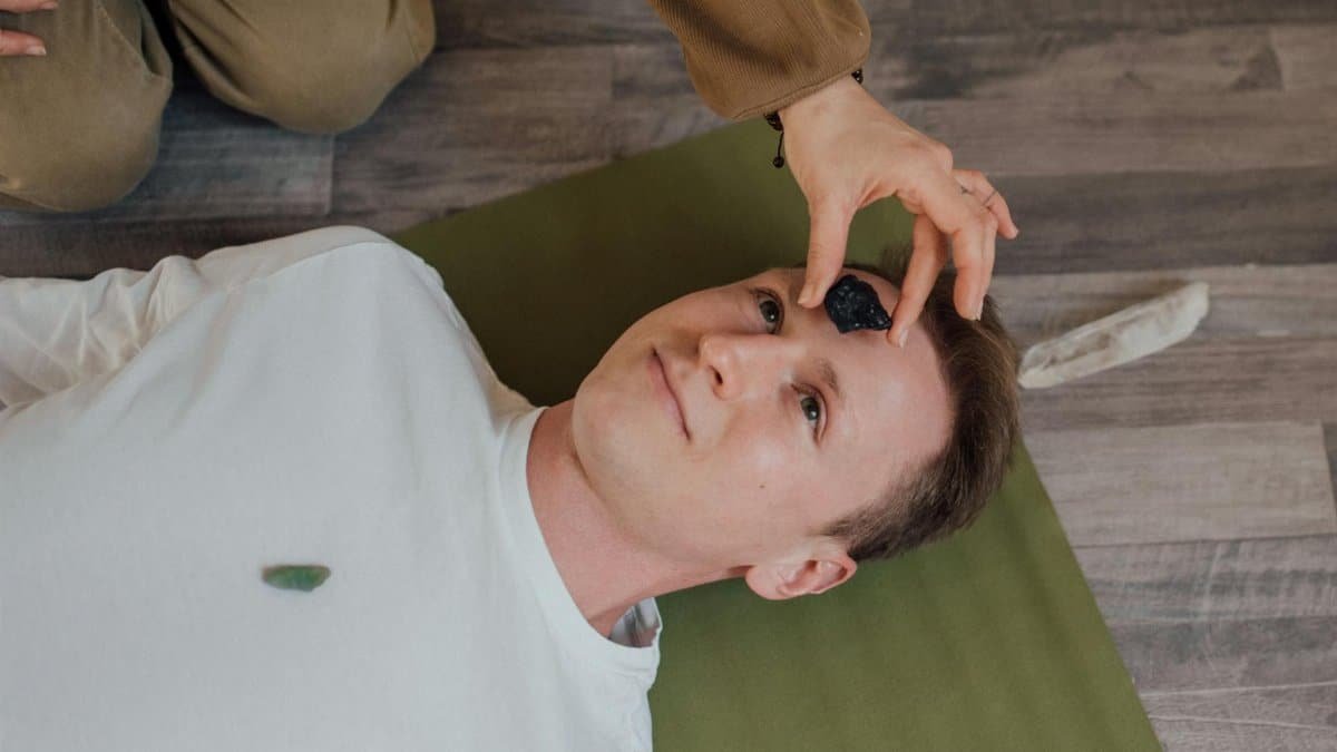 A man lying down during a crystal healing ritual indoors on a yoga mat.