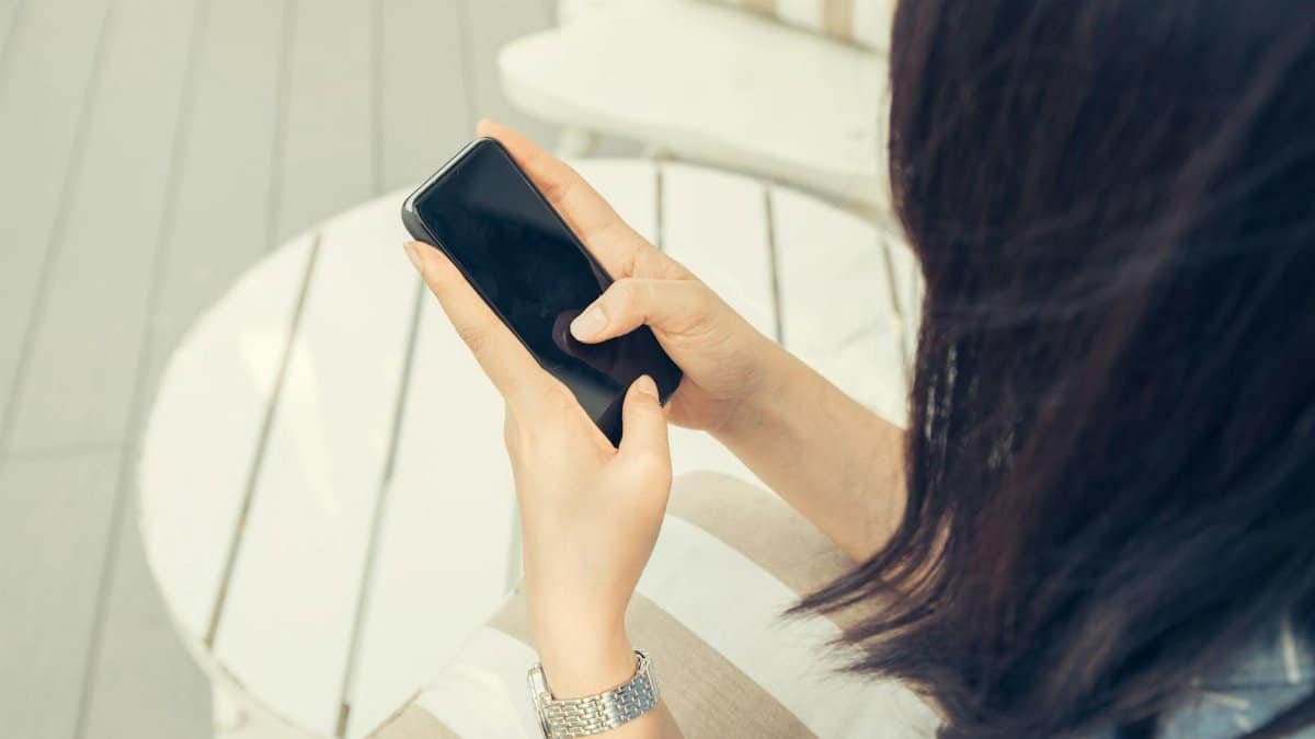Woman using a smartphone while sitting outdoors on a sunny day.