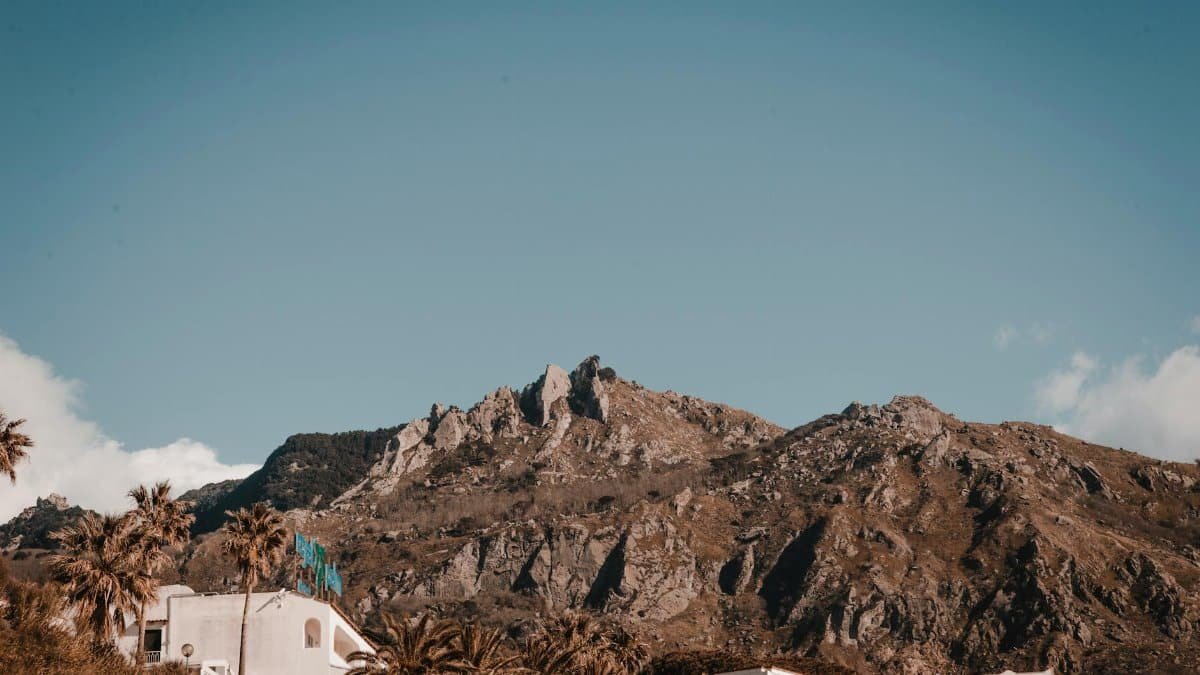 Stunning view of rocky mountain under clear sky with houses and palm trees in foreground.