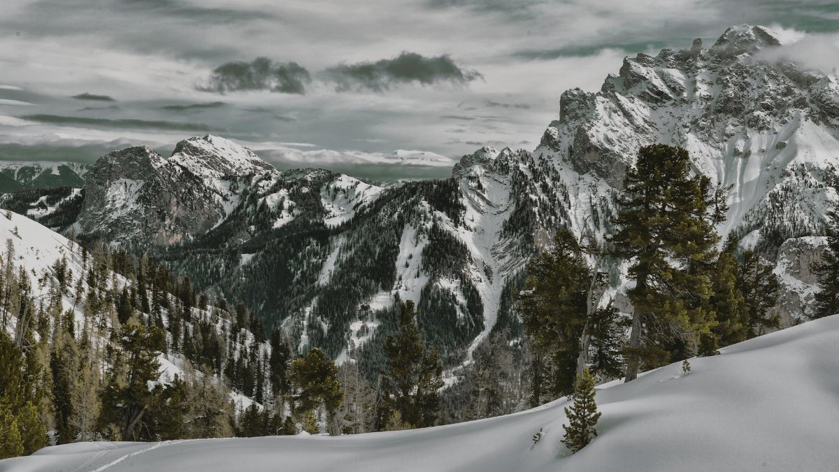 Breathtaking winter mountain scene with snow, trees, and a dramatic sky.