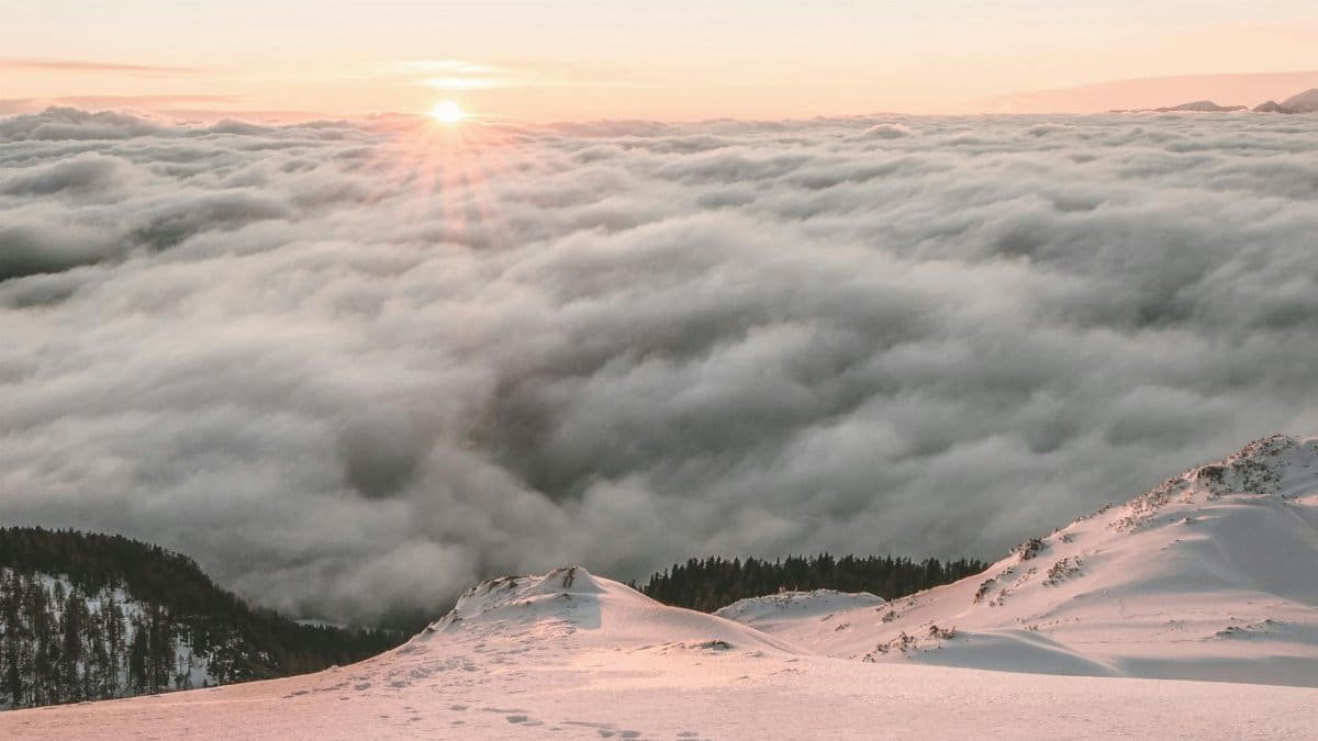 Breathtaking view of sunrise over a snow-covered mountain and a sea of clouds, capturing nature's serene beauty.