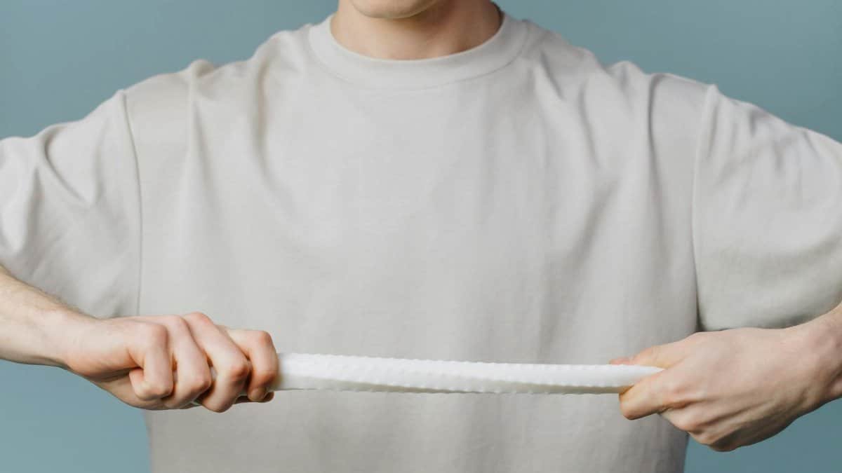 Close-up of a man stretching a textured white band against a blue background, showcasing minimalist style and tension concept.