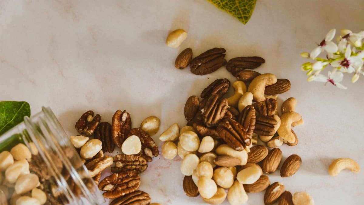 A close-up of mixed nuts spilled from a jar, featuring pecans, cashews, and almonds on a marble surface.