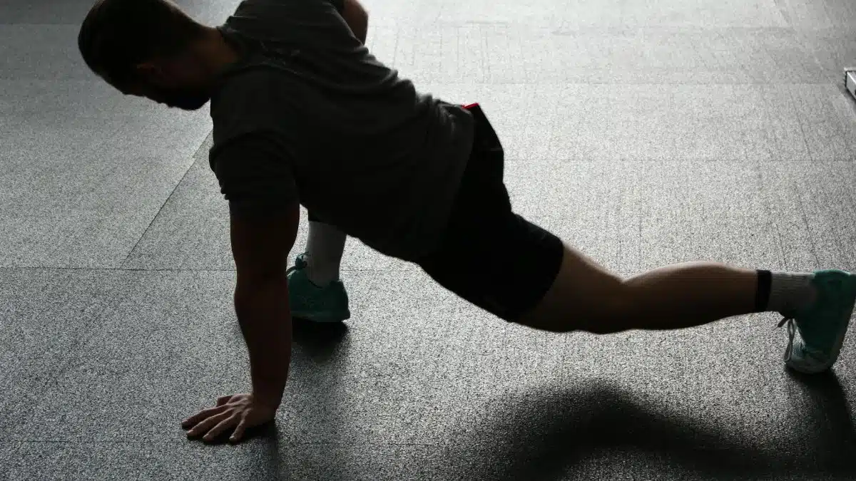 Silhouette of a man executing a stretching routine in a dim gym environment.