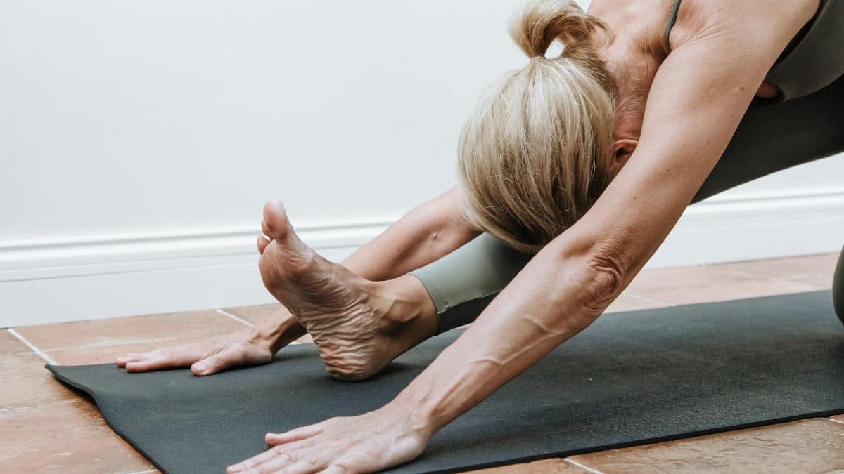 An adult woman performs a yoga stretch indoors on a mat, showcasing fitness and flexibility.