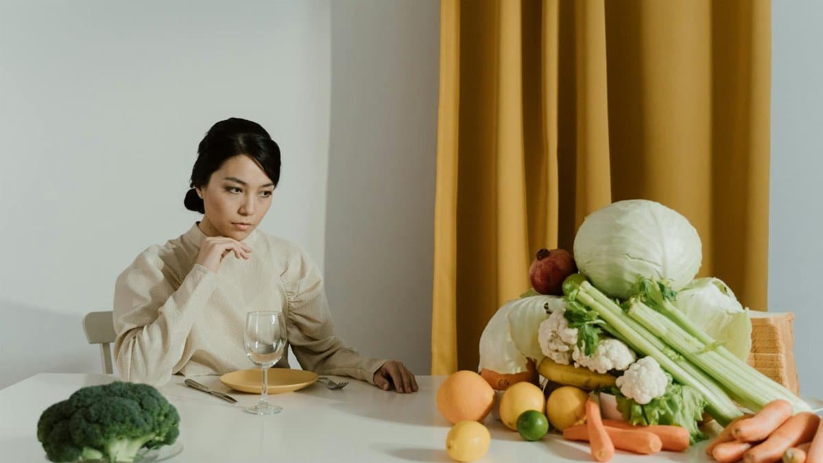 A woman seated at a table with a variety of fresh vegetables, representing healthy eating.