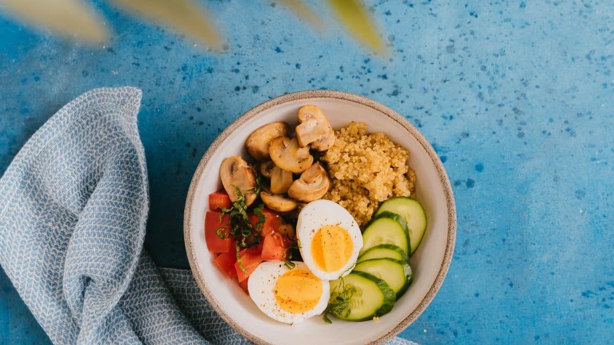 A delicious and healthy breakfast bowl featuring quinoa, boiled eggs, vegetables on a blue background.