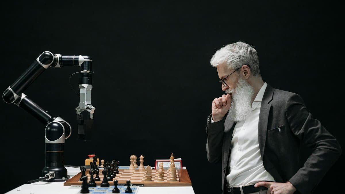 An elderly scientist contemplates a chess move against a robotic arm on a chessboard.